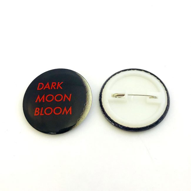 Black button badge with red writing front and back